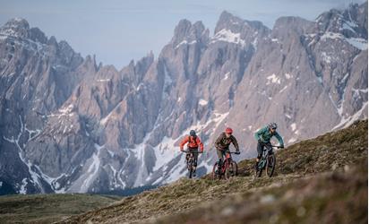 Three cyclists on a mountain trail in front of a striking rock formation.