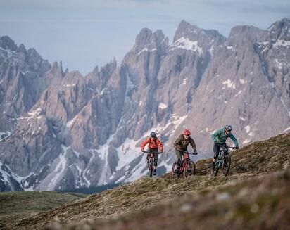 Drei Radfahrer auf einem Bergpfad vor einer markanten Felslandschaft.